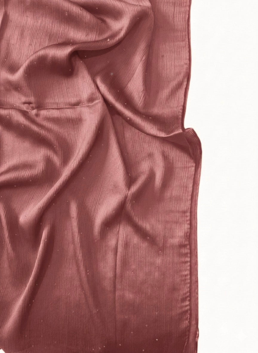 A Luxe Crinkle Silk Hijab in Teapink drapes elegantly, showcasing its textured crinkle fabric and soft sheen.